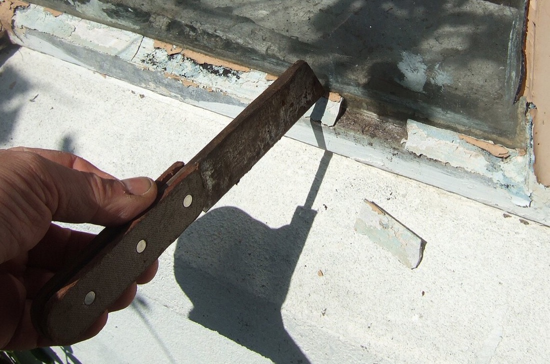 A hacking knife held against the putty line of a window frame, chopping out the old fillet.